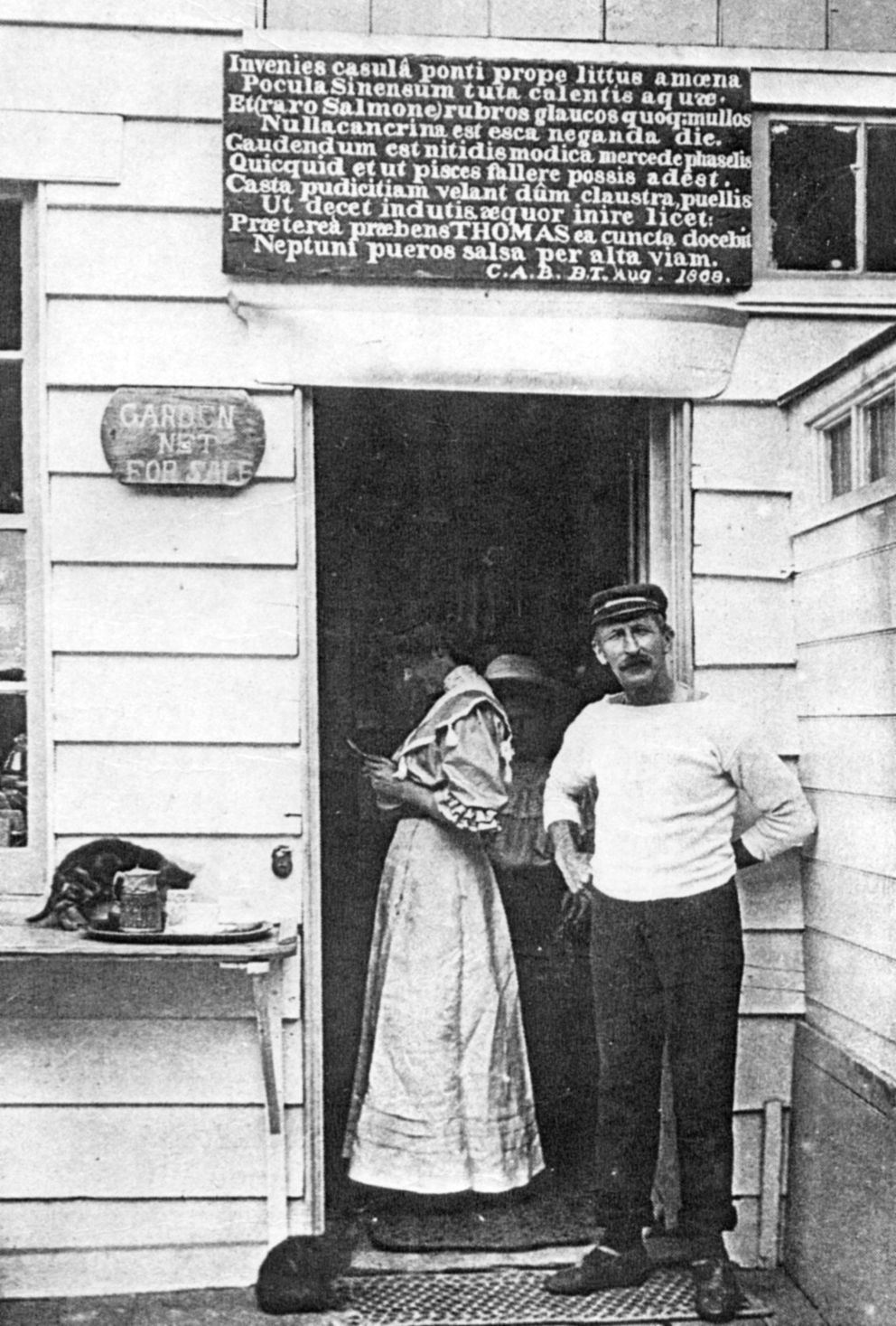 old photograph of Thomas standing at the door of his café with the Latin sign.
